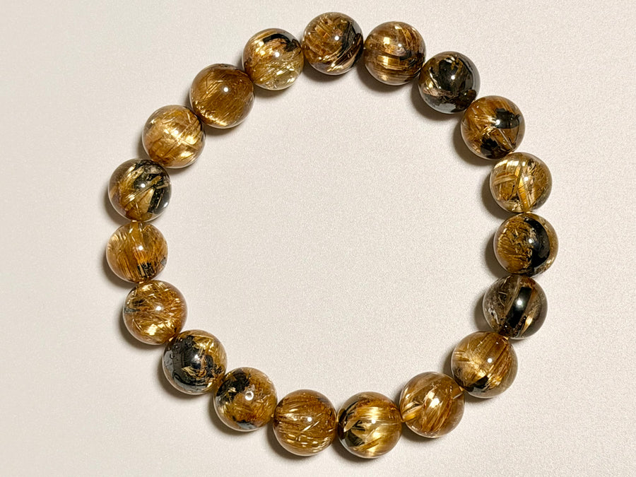 上から撮影した太陽花タイチンルチルクォーツ11-11.5mm。粒ごとの針の入り方や黒い表情、全体の配色バランスが確認できます。