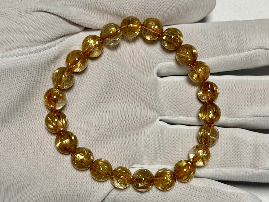 手袋着用で持ったタイチンルチルクォーツ8.5-9mm。金紅石入り水晶のゴールド針と粒ごとの表情を確認できます。