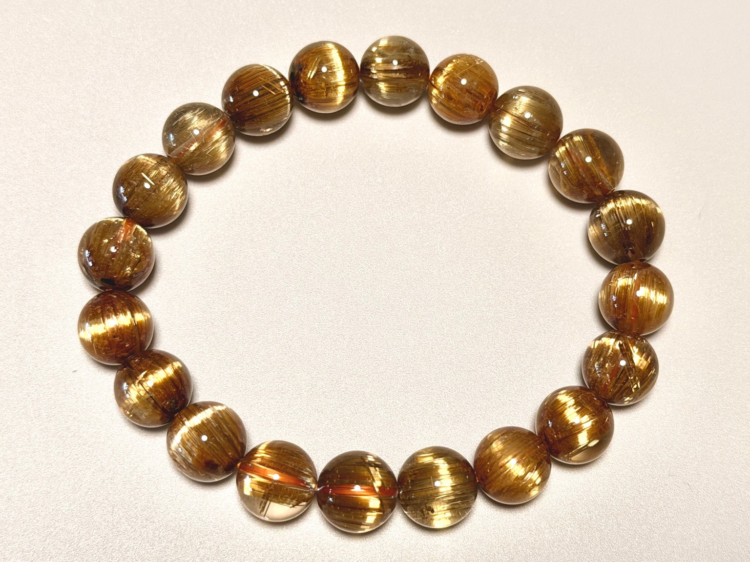角度を変えて撮影したキャッツアイタイチンルチルクォーツ9.5-10mm。粒ごとの黄金針、キャッツアイ状の光、透明感を確認できます。