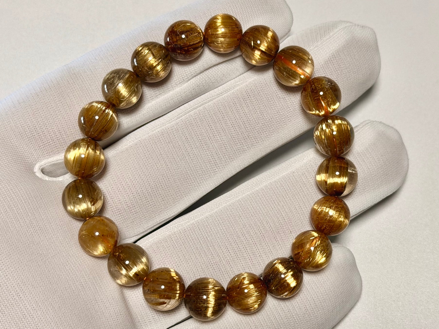 白手袋の上で撮影したキャッツアイタイチンルチルクォーツ9.5-10mm。粒サイズと黄金針の入り方、一周の表情を確認できます。